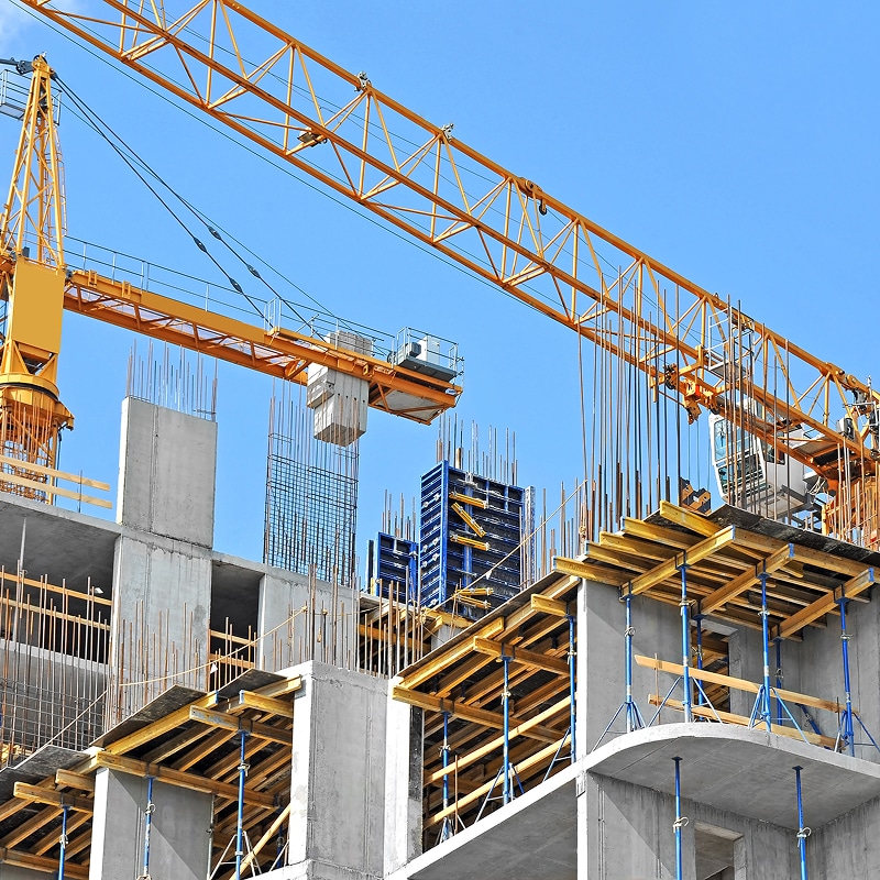Chantier de construction avec une grande grue jaune dominant un bâtiment en béton armé en cours de construction sous un ciel bleu.