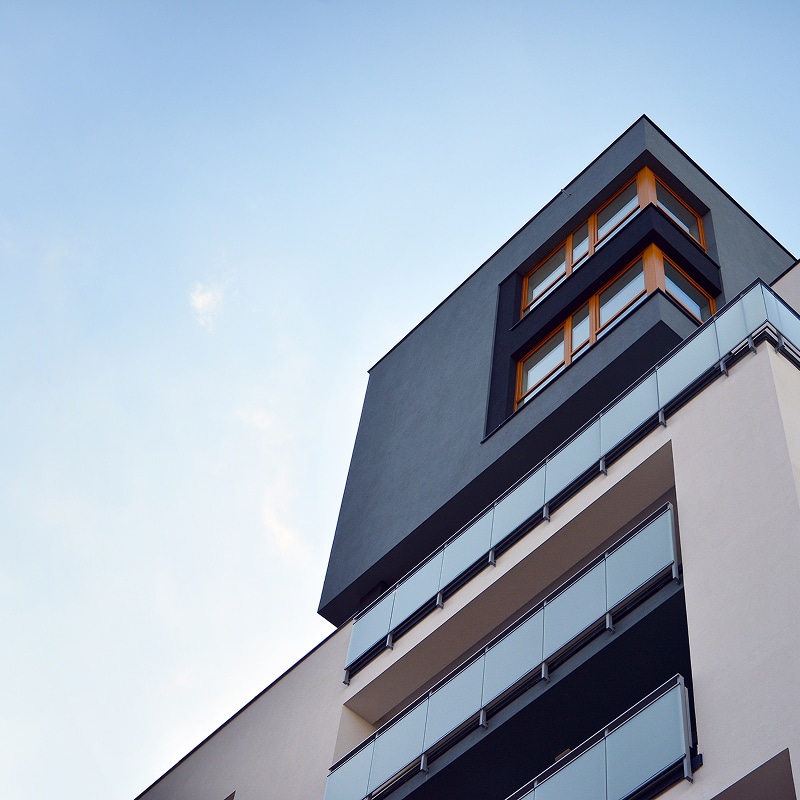 Façade moderne d'un immeuble d'appartements gris et blanc, avec balcons vitrés et fenêtres à cadre bois sous un ciel bleu clair.