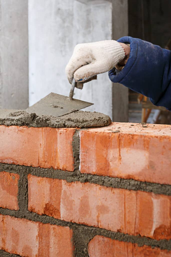Main gantée appliquant du mortier avec une truelle sur des briques rouges. Construction d'un mur en maçonnerie sur chantier.